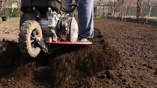 Senior Man Farmer working in the garden plows with Garden Tiller