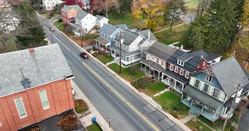 Aerial establishing shots of colorful homes along road in USA. Church building and traffic drives by
