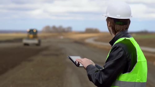 The Engineer Looks at the Construction Plan on the Tablet and Examines the Process of Construction