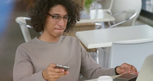 Young Man Working on Laptop and Phone in Cafe