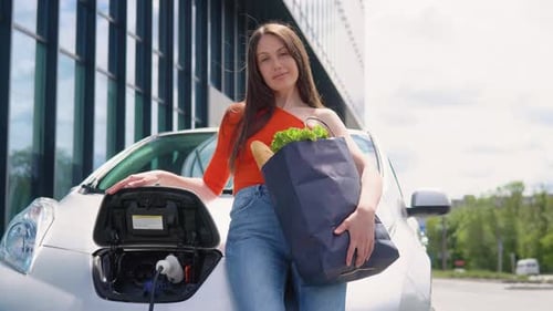 Mujer de pie junto al coche eléctrico con comestibles