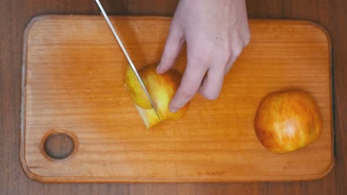 Woman Hands with a Knife Sliced Apple on a Wooden Kitchen Board in a Home Kitchen