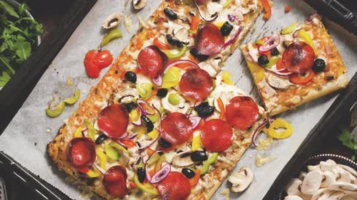 A Piece of Square Pizza with Basil Pepperoni Tomatoes and Mushrooms on a Iron Tray