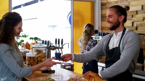 Cafe scene with cheerful barista handing drink to customer