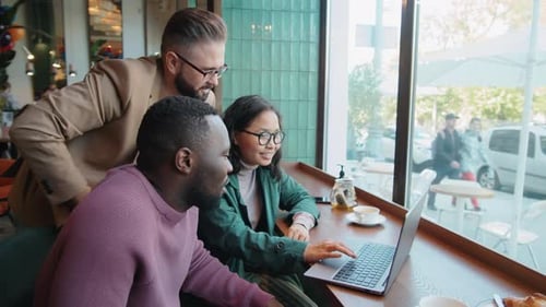 Multiethnic Colleagues Using Laptop and Discussing Project in Cafe