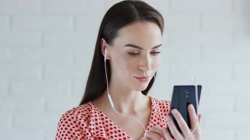 Woman Using Cell Phone with Earbuds Indoors