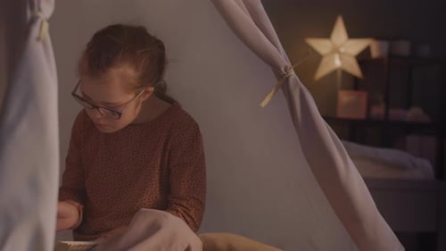 Girl Reading Book in Dark in Tent at Home