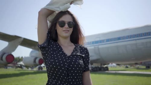 Linda garota morena com o xale branco e óculos na frente do avião grande e olhando para a câmera