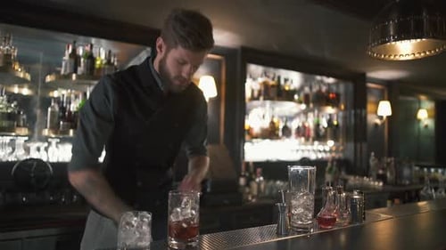 Handsome Bartender Adding Big Cubes of Ice Making a Whiskey Cocktail in Beautiful Modern Bar
