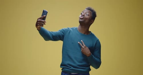 Young Adult Taking Selfies with Phone on Yellow Background
