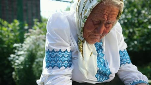 An Old Grandmother is Sitting on the Street and Reading a Book