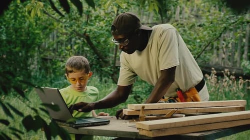 Young Boy Uses Laptop with Adult Carpenter