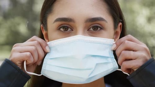 Young Woman Puts on Surgical Mask Outdoors