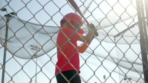 Boy Hitting Baseball in Batting Cage on Sunny Day