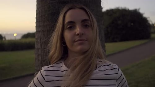 Slow motion shot of young blond woman leaning on tree trunk in park