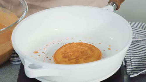 Golden Pancake Cooking in a White Frying Pan
