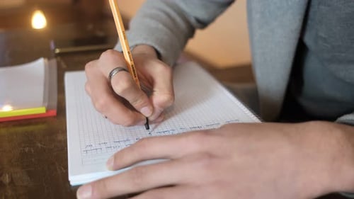 Person Writing in Notebook with a Pencil