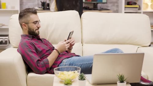 Bearded Man Relaxing on Couch Using Mobile Phone