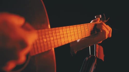 Spielen einer Akustikgitarre mit roter Hintergrundbeleuchtung und schwarzem Hintergrund