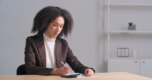 Afroamerikanische Buchhalterin mit lockigen Haaren sitzt am Bürotisch verwendet Taschenrechner zum Planen