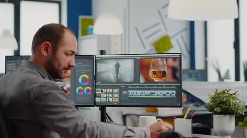 Man Editing Video Footage on Dual Monitors