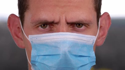 Young Man in a Medical Protective Face Mask Looking at the Camera on the Street Background