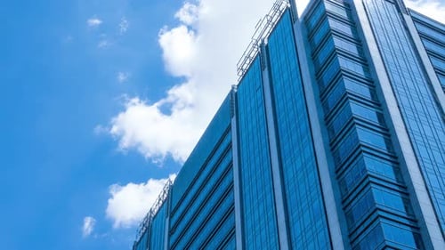 Zeitraffer, Blick auf einen glasbedeckten Wolkenkratzer, der den blauen Himmel und vorbeiziehende Wolken reflektiert