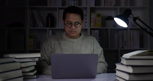 young man working on laptop in dimly lit library room