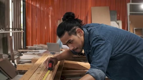 Carpenter Measures Lumber in Workshop With Assistant