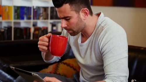 Man Uses Tablet While Drinking Coffee At Home