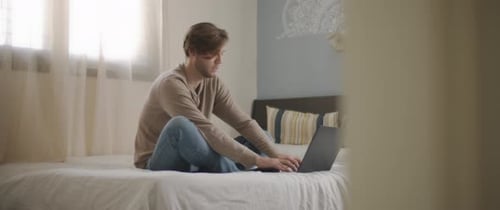 Young Adult Using Laptop in Bedroom