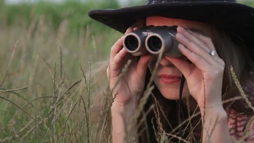 Woman with Binoculars Crouching in Rural Field