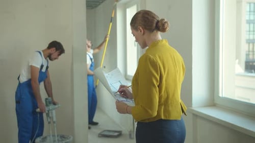 Woman Watches How Builders Work and Amends a Drawing