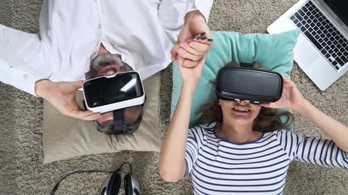 Couple Wearing VR Headsets Lying on Rug