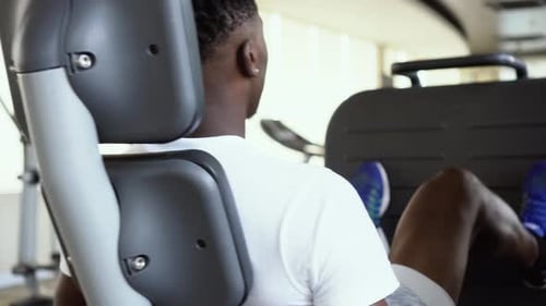 Back View of African American Man Doing Exercise on Leg Press During Fitness Training in Modern Gym