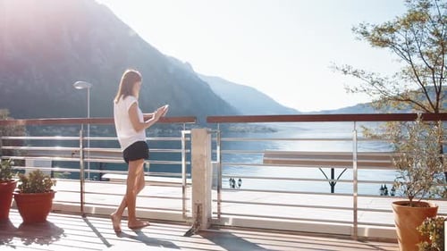 Woman on Balcony Looking at Phone by the Sea