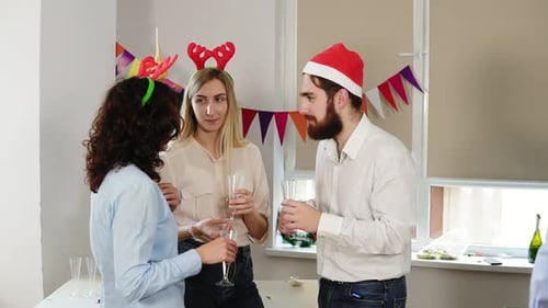 Jovens trabalhadores de escritório conversando e segurando copos com vinho espumante durante a festa de Natal no