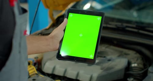 Car Service Manager or Mechanic Uses a Tablet Computer with a Green Screen Mock Up That Is Pointed