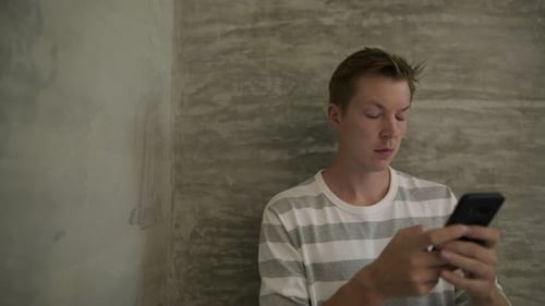 Young Adult Using Smartphone Indoors by Gray Wall