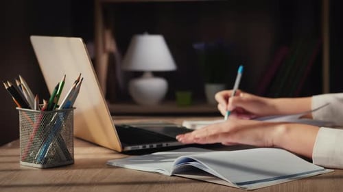 A Woman's Hand Writes in a Notebook Sitting Near a Laptop at Home