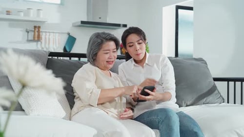 Two Women Look at Smartphone and Laugh on Couch