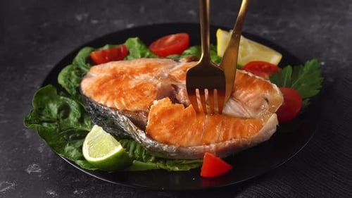 Nahaufnahme eines gegrillten Lachssteaks in einem schwarzen Teller mit Salatblättern