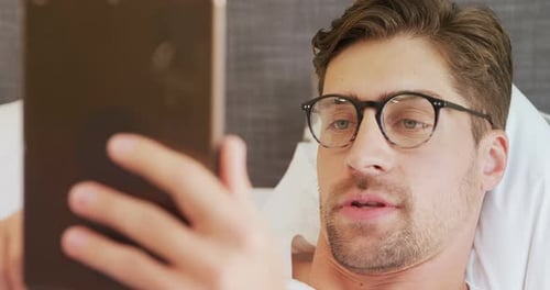 Man Lies in Bed While Looking at Tablet