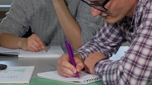 People Writing in Notebooks at Table Indoors