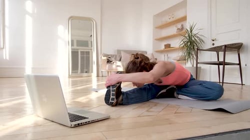 La mujer se dobla hacia adelante según un vídeo tutorial en el suelo