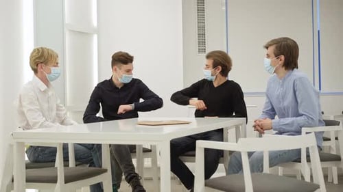 Positive Millennial Coworkers in Coronavirus Face Masks Touching Elbows Making Deal in Office
