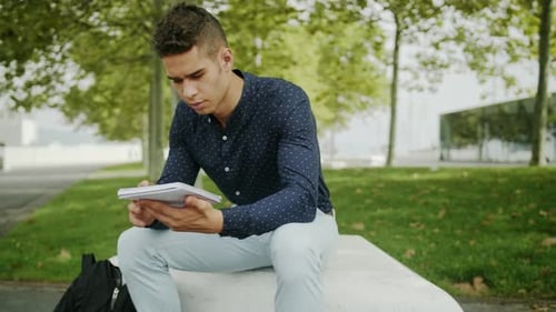 Well-Dressed Portrait Young Attractive Trendy Man reading and taking notes on a urban park sunny mor