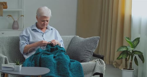 Focused Mature Adult Woman Holding Needles Spending Time at Home with Knitting Resting with Hobby