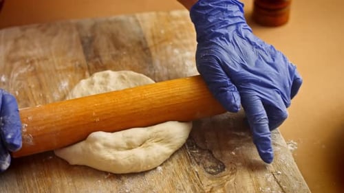 Hands Rolling Dough on Wood Cutting Board