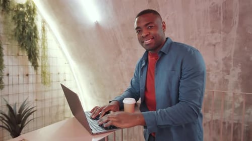 Joyeux homme noir posant à un bureau debout dans un espace de coworking